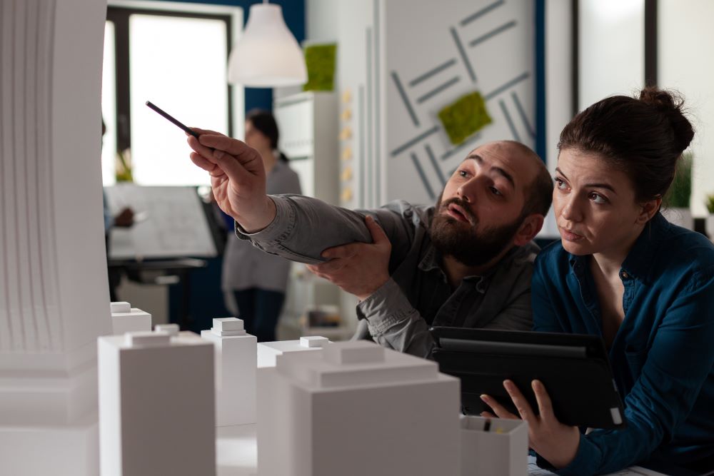 Deux architectes au bureau réfléchissent à partir de la maquette d’un bâtiment.